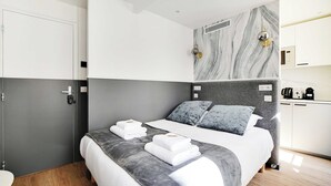 A modern hotel room with a bed, grey and white walls, a marble-patterned accent wall, and a small kitchenette. - Cosy Studio for 2P with A/C - Near Montmartre (Paris)