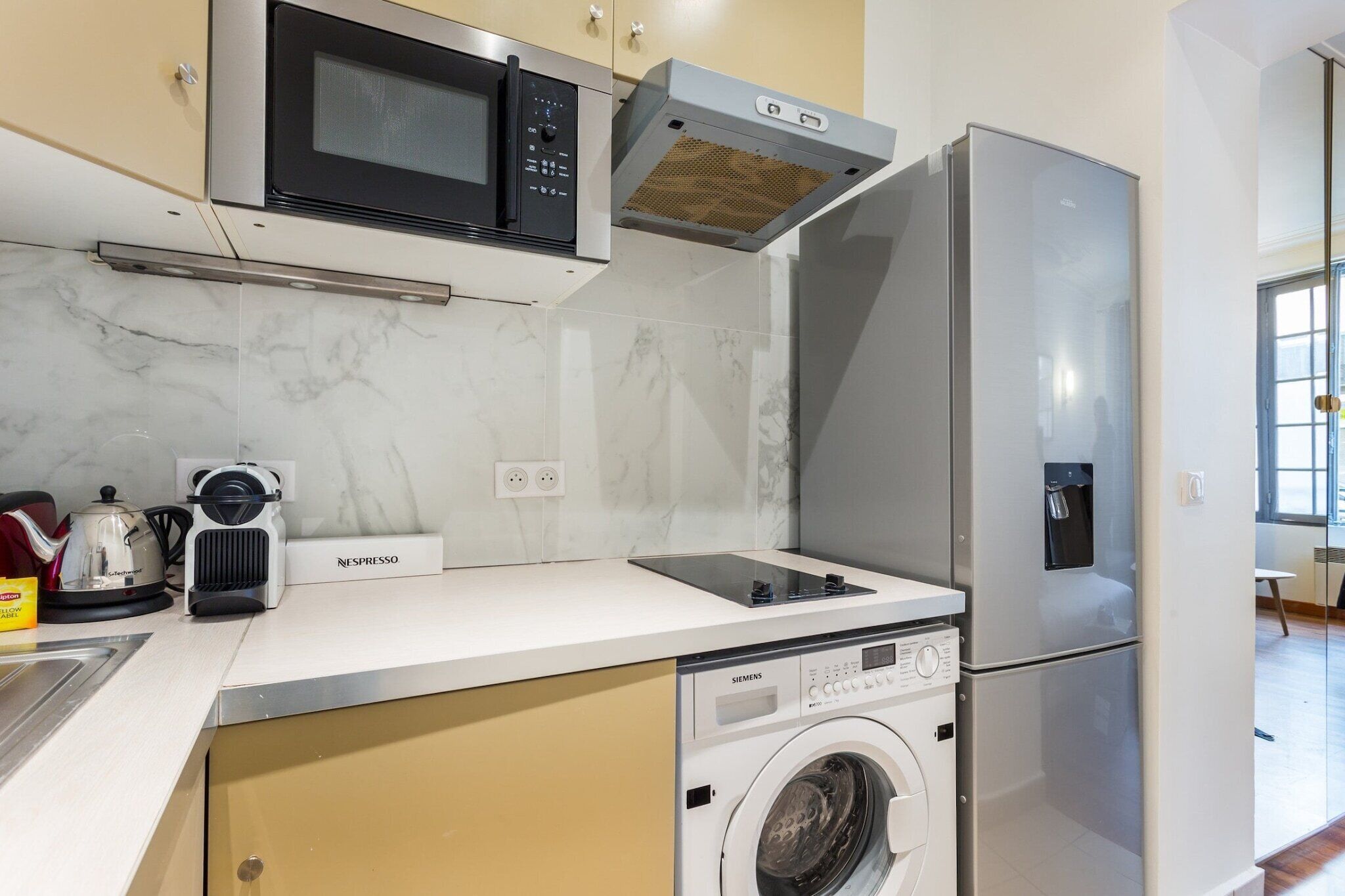 A compact kitchen with a microwave, espresso machine, and a Siemens washing machine.