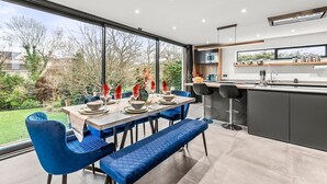 A modern kitchen with a large window, a dining area with blue upholstered chairs, and a bar area.