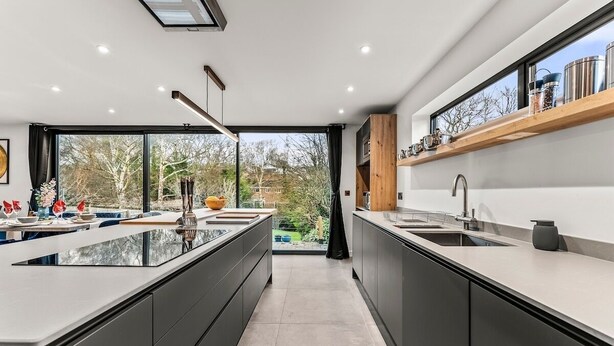 A modern kitchen with a large island, dark cabinetry, and a view of the outdoors.