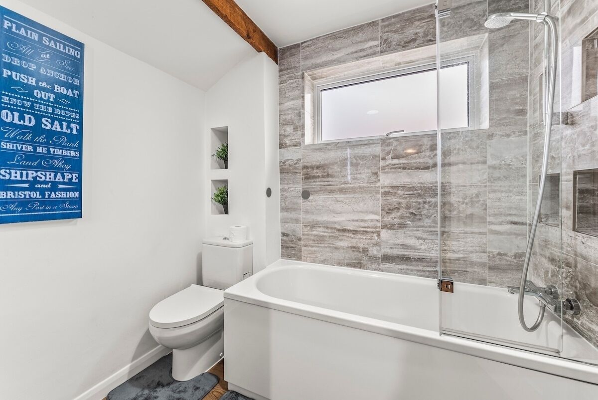 Een moderne badkamer met een vrijstaand bad, een douche met glazen wand en een toilet.