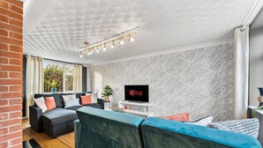 A modern living room with a sectional sofa, a flat-screen TV displaying 'NETFLIX', and a patterned wall. - Boutique Cambridgeshire Gem (Cambridge)