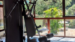Une salle de sport équipée d’un appareil d’exercice de la marque KIKO, de grandes fenêtres offrant une vue sur la verdure et de carreaux de sol à motifs.