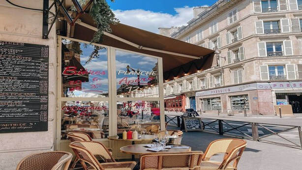 An outdoor café with wicker chairs and tables, a menu board, and a view of the street. - Charming studio - 2P- Le Marais (Paris)