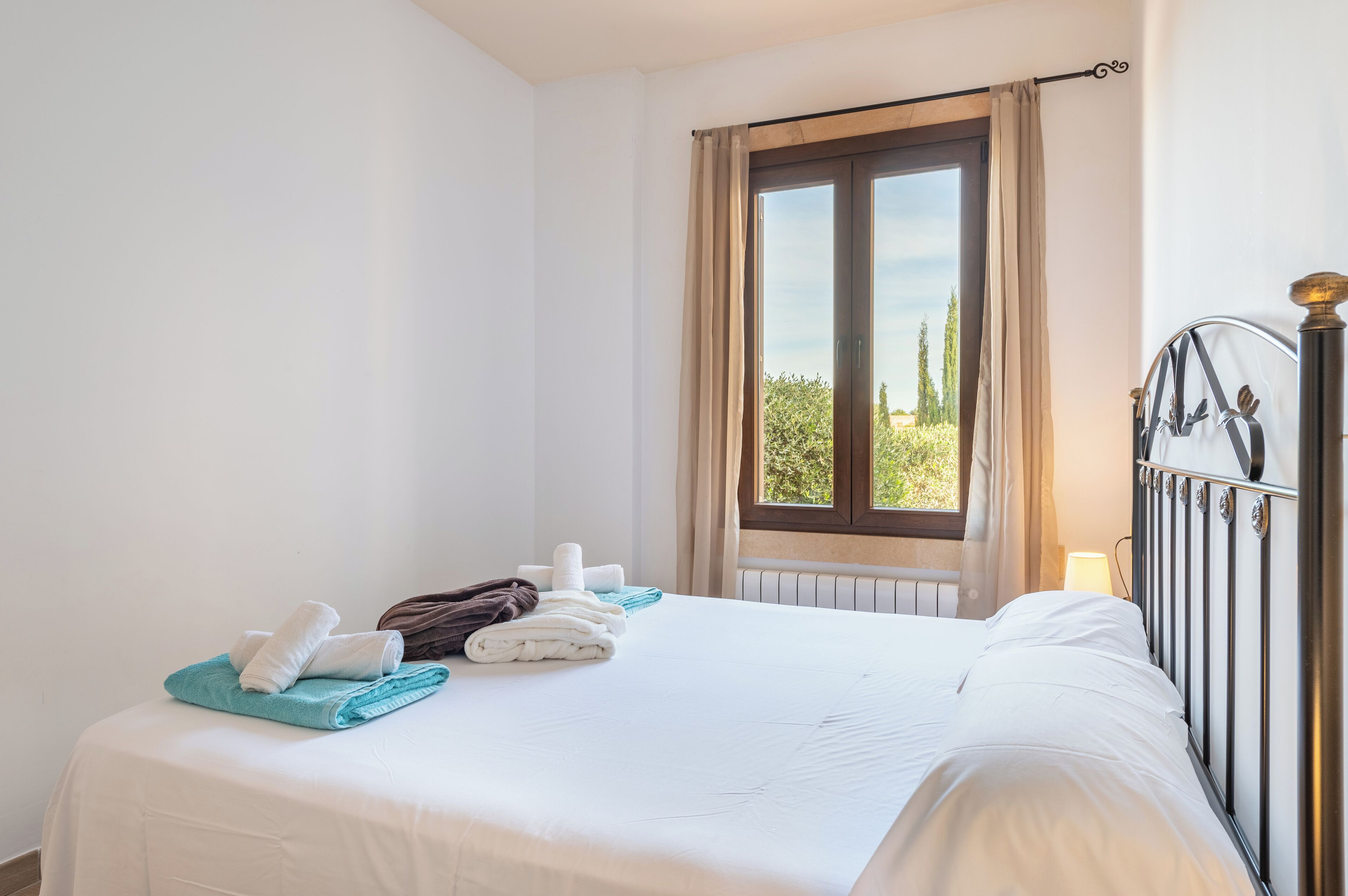 A neatly made bed with towels and a view of greenery outside.