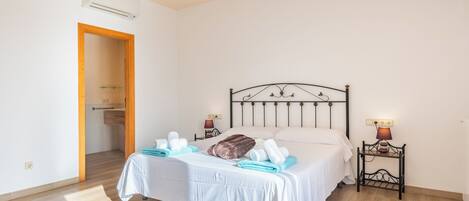 Un lit bien fait, avec du linge de lit blanc et un oreiller marron, une table de chevet avec une lampe, et une porte en bois donnant sur une salle de bain.