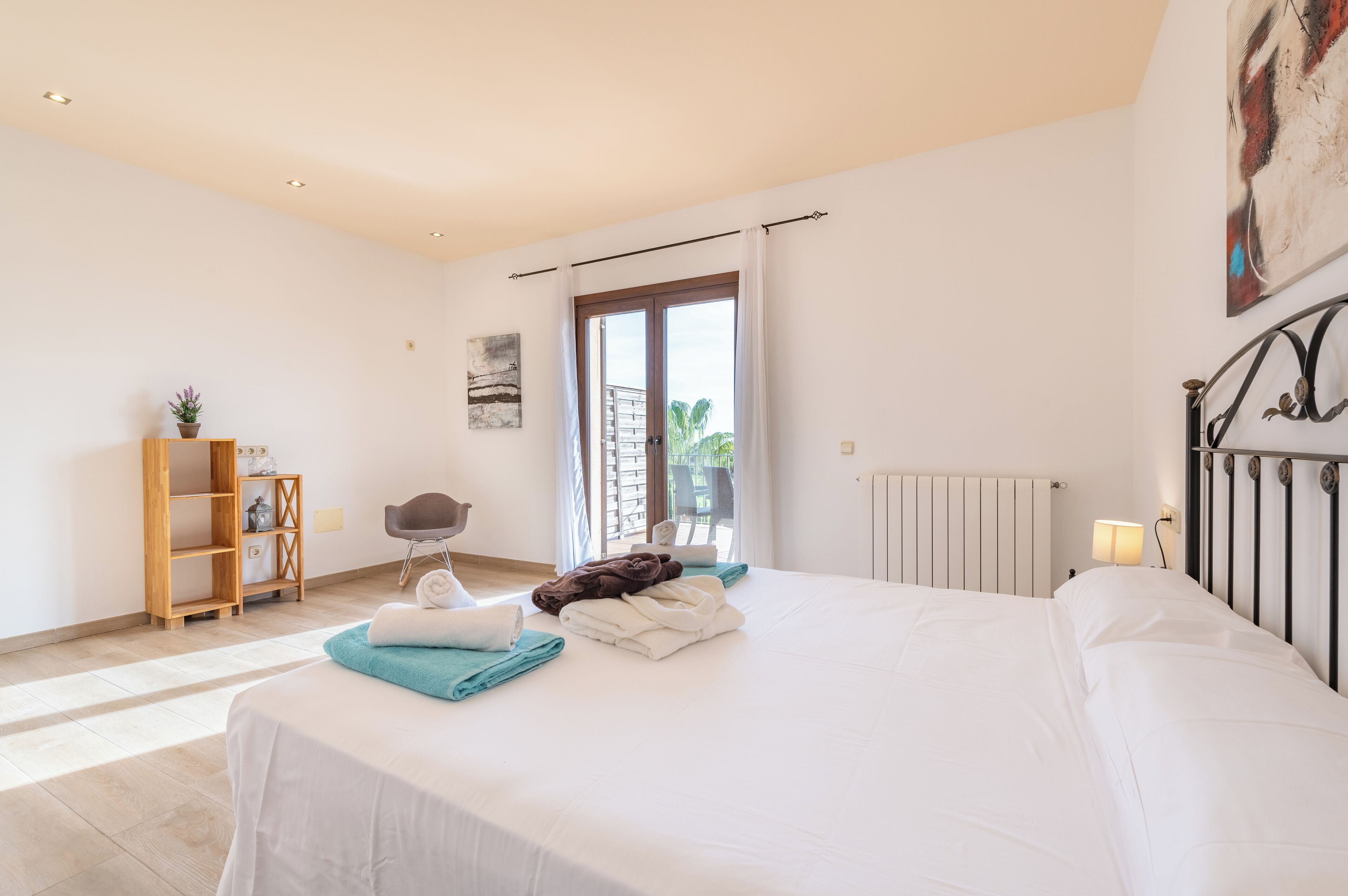 Une chambre à coucher avec un lit, une étagère en bois ornée d’une plante, une chaise et une fenêtre avec des rideaux.