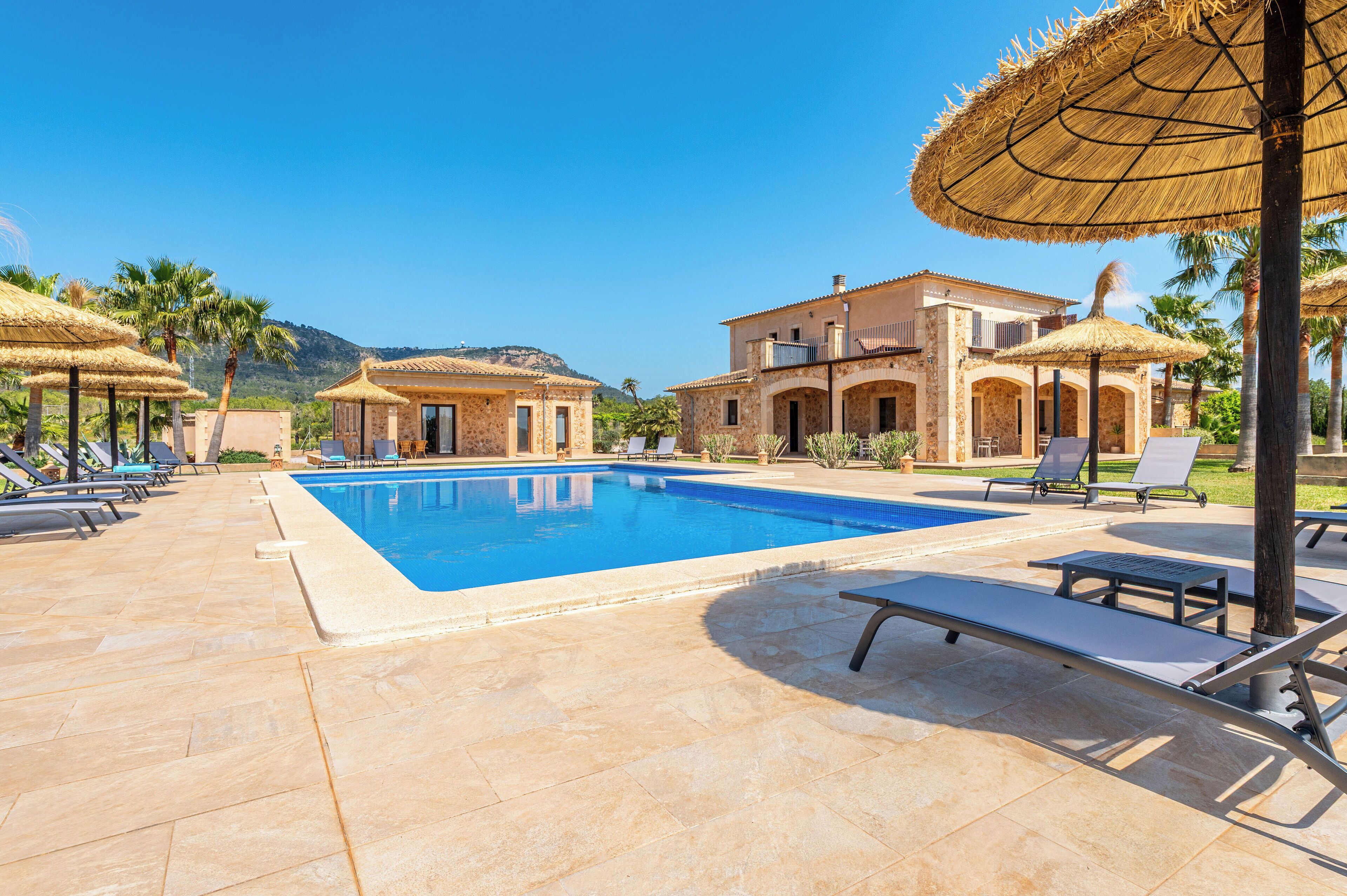 Zona de piscina amb gandules i ombrel·les, una piscina blava i cristal·lina, i un edifici amb balcó.