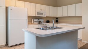 A modern kitchen with white cabinets, a built-in microwave, a stainless steel sink, and a refrigerator. - Charming townhome in brilliant Bethel, close to Sunday River. (Bethel)