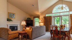 A living room with a fireplace, sofa, TV, and dining table with chairs. - Charming townhome in brilliant Bethel, close to Sunday River. (Bethel)