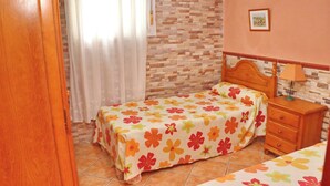 A bedroom with a bed, a nightstand, a lamp, a window with curtains, and a brick-patterned wall. - Apartamento Manolete (Conil de la Frontera)
