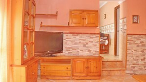 A kitchen with wooden cabinets, a tiled backsplash, and a television on a wooden stand. - Apartamento Manolete (Conil de la Frontera)