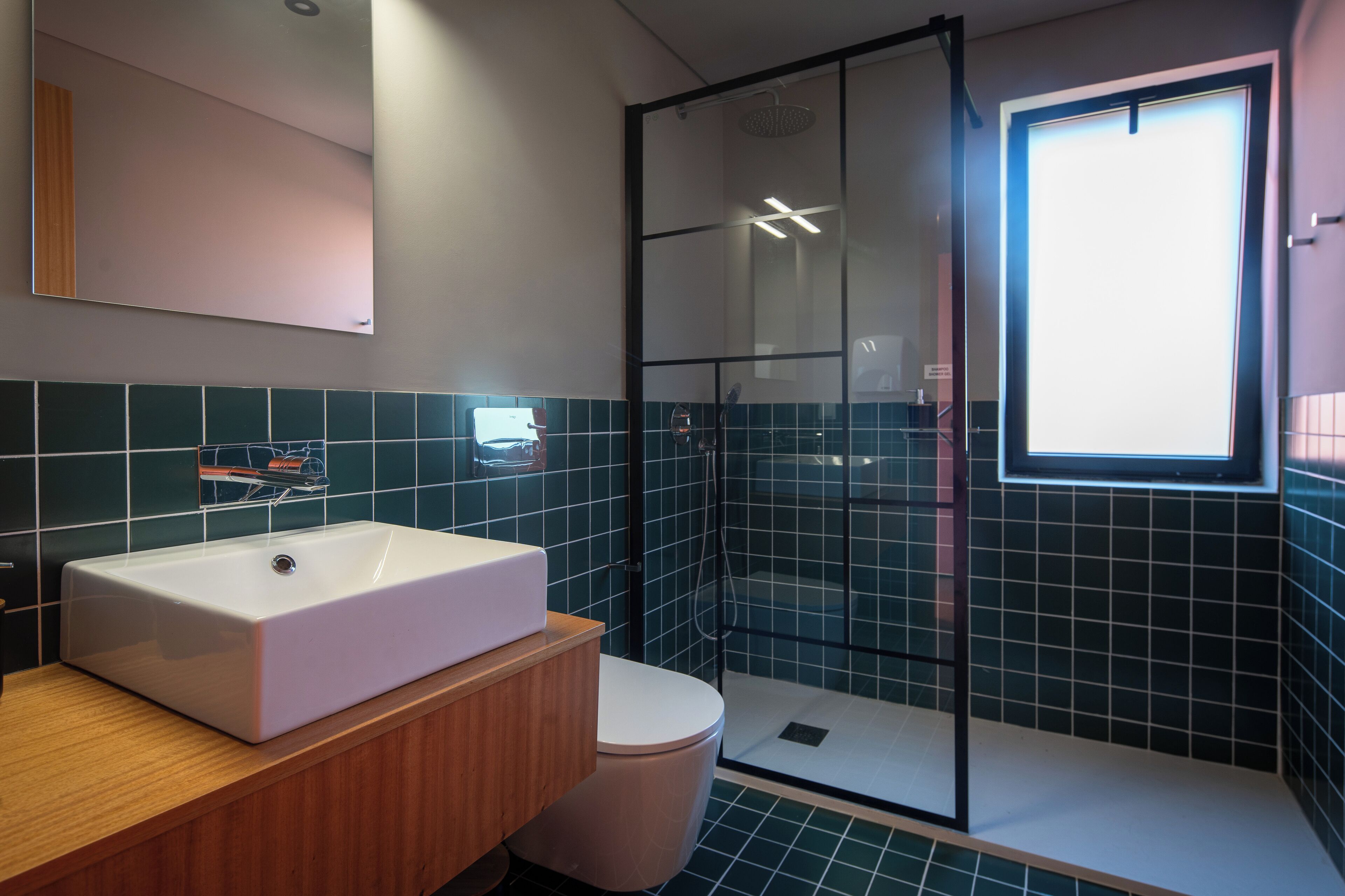 Un baño moderno con un lavamanos grande de color blanco, un inodoro y una zona de ducha con mampara de vidrio.