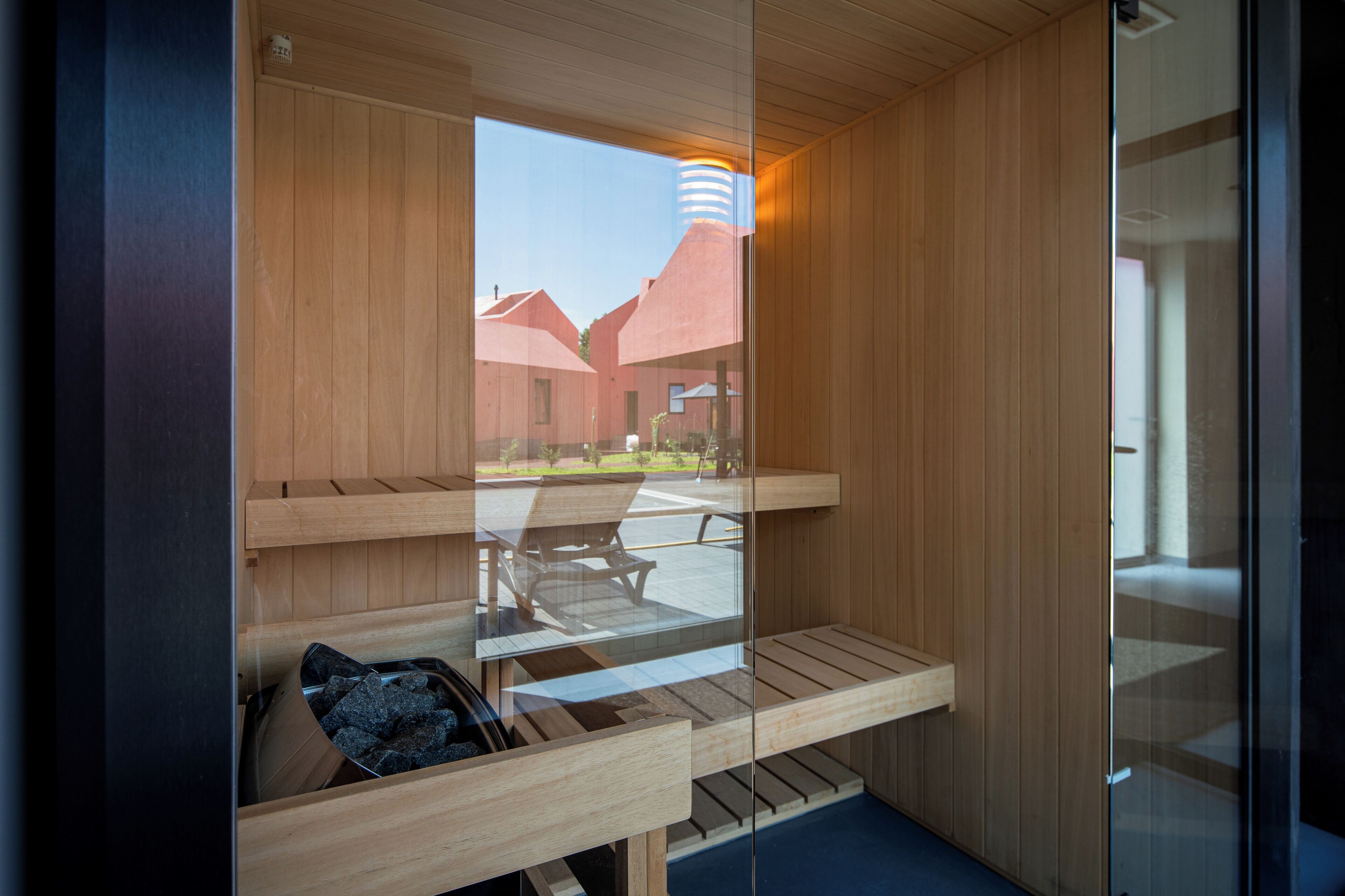 A sauna with wooden benches and a glass door, offering a view of buildings in the background.