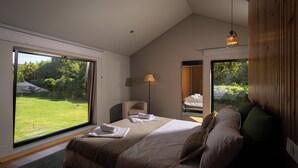 A modern bedroom with a large bed, a chair, a lamp, and a view of a garden through a large window. - Canto's Green Garden & SPA  (Povoacao)