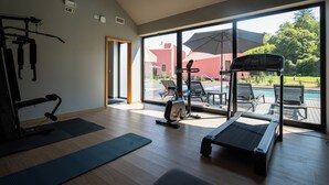 A modern gym with exercise equipment, large windows, and a view of a pool and outdoor seating. - Canto's Green Garden & SPA  (Povoacao)