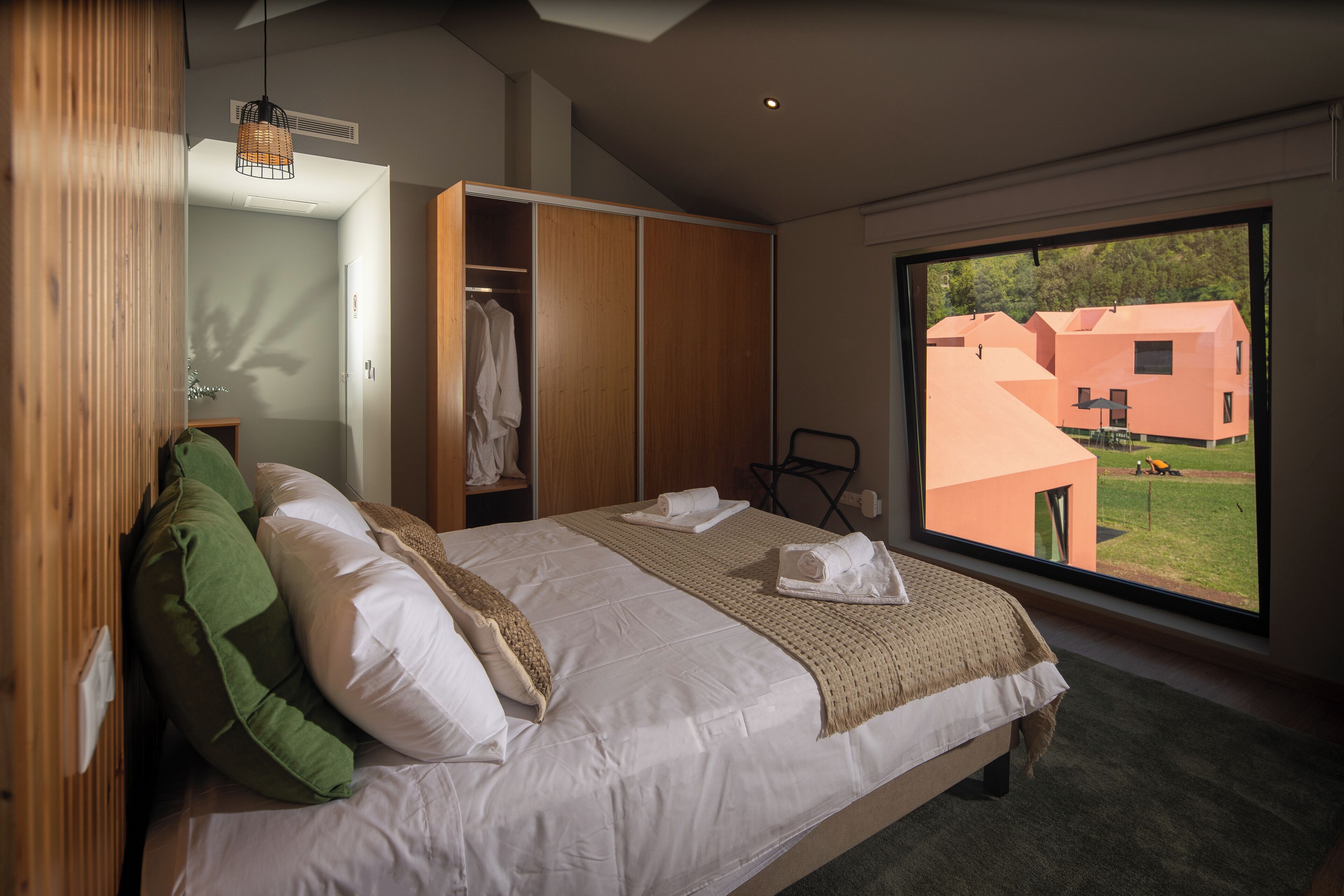 Ein modernes Schlafzimmer mit einem großen Bett, einem Kleiderschrank und Blick auf ein Gebäude.