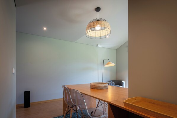 Comedor con mesa de madera, sillas traslúcidas, una lámpara colgante de fibra y una lámpara de pie, además de una cesta pequeña.
