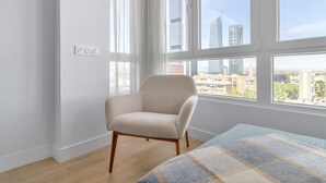 Una habitación con un ventanal grande, un sillón color beige y una manta escocesa sobre la cama.