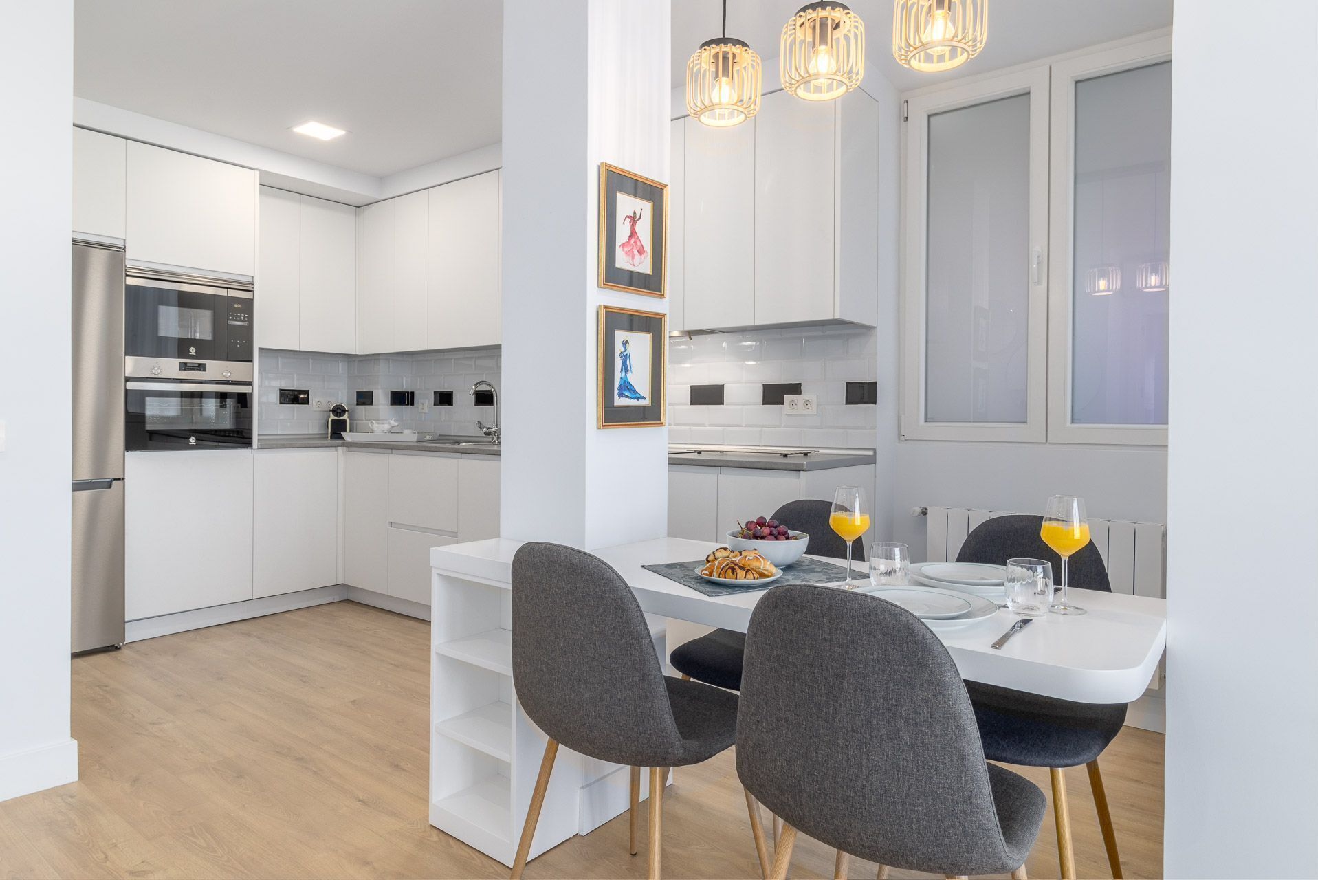 A modern kitchen with white cabinetry, a built-in oven, and a dining area with a white table and grey chairs.