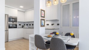 Una cocina moderna con armarios blancos, horno empotrado y un comedor con mesa blanca y sillas grises.