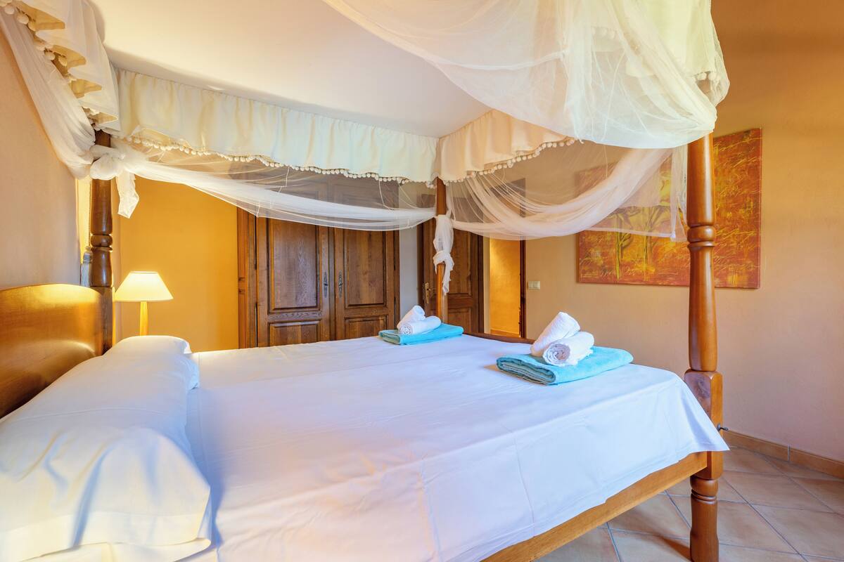 A neatly made bed with white linens, a wooden headboard, and a canopy.