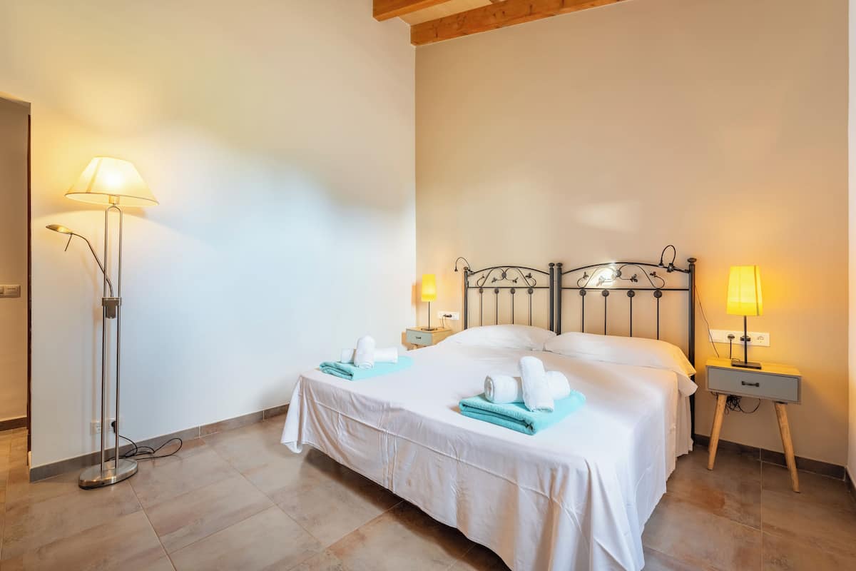 A hotel room with a double bed, two bedside tables with lamps, a floor lamp, and towels on the bed.