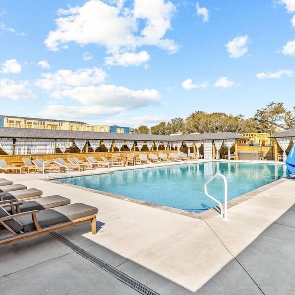 A pool area with lounge chairs, a pool, and a covered seating area.