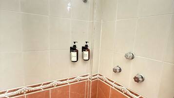 A bathroom with beige and brown tiles, a shower with a green head, and two bottles of shampoo and body wash.