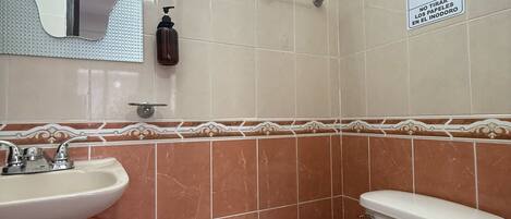 A bathroom with a sink, mirror, toilet, and hand sanitizer dispenser.