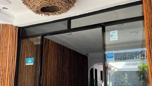 Ein moderner Hotelzugang mit Glastür, einer Hängeleuchte mit Gewebekuppel und einem Schild, das den Eingang weist.