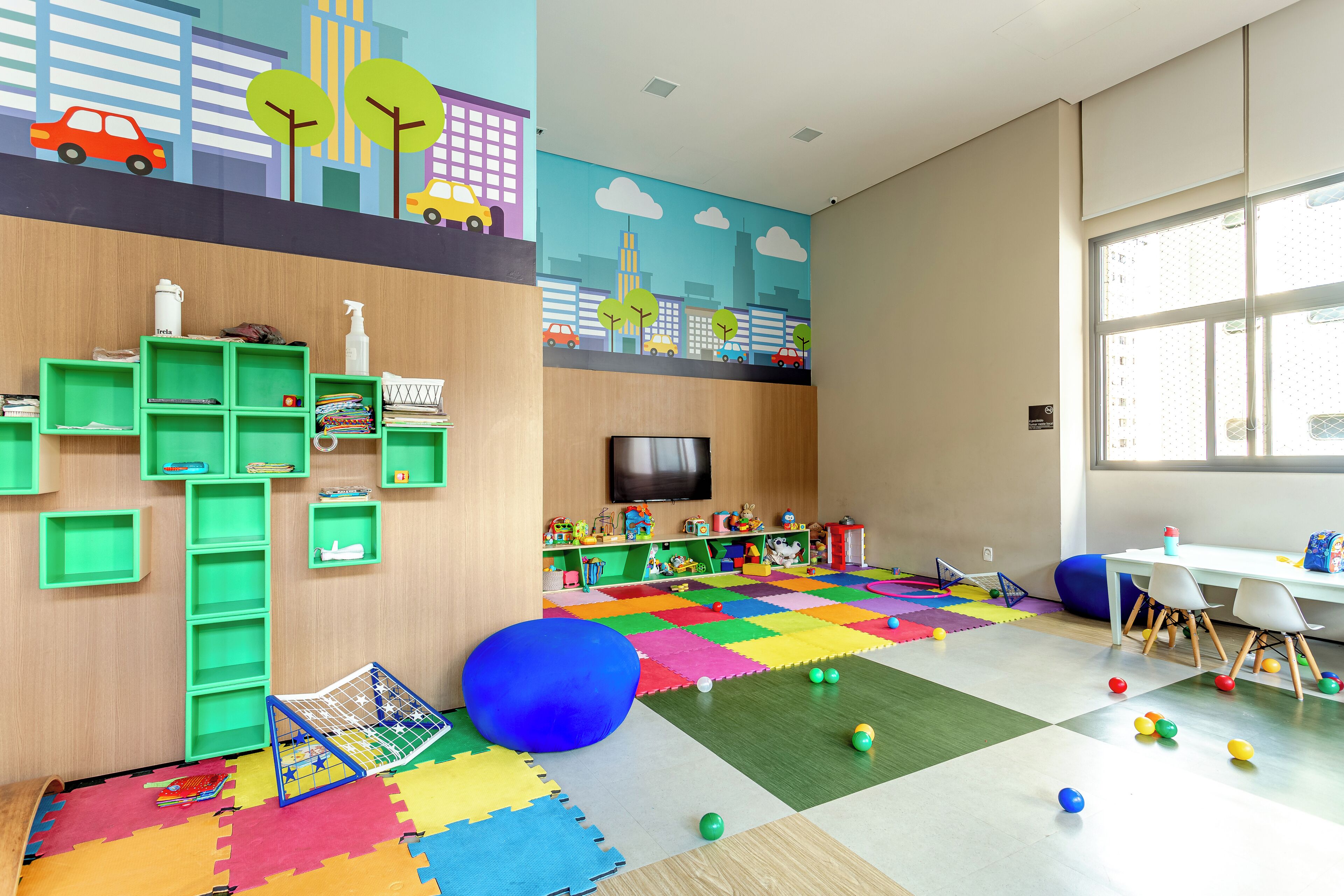 A children's playroom with colorful foam mats, a blue ball, and green storage units.