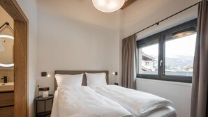 En välordnad dubbelsäng i ett hotellrum med en sänggavel i trä, ett litet nattduksbord med en vas och ett fönster med gardiner.