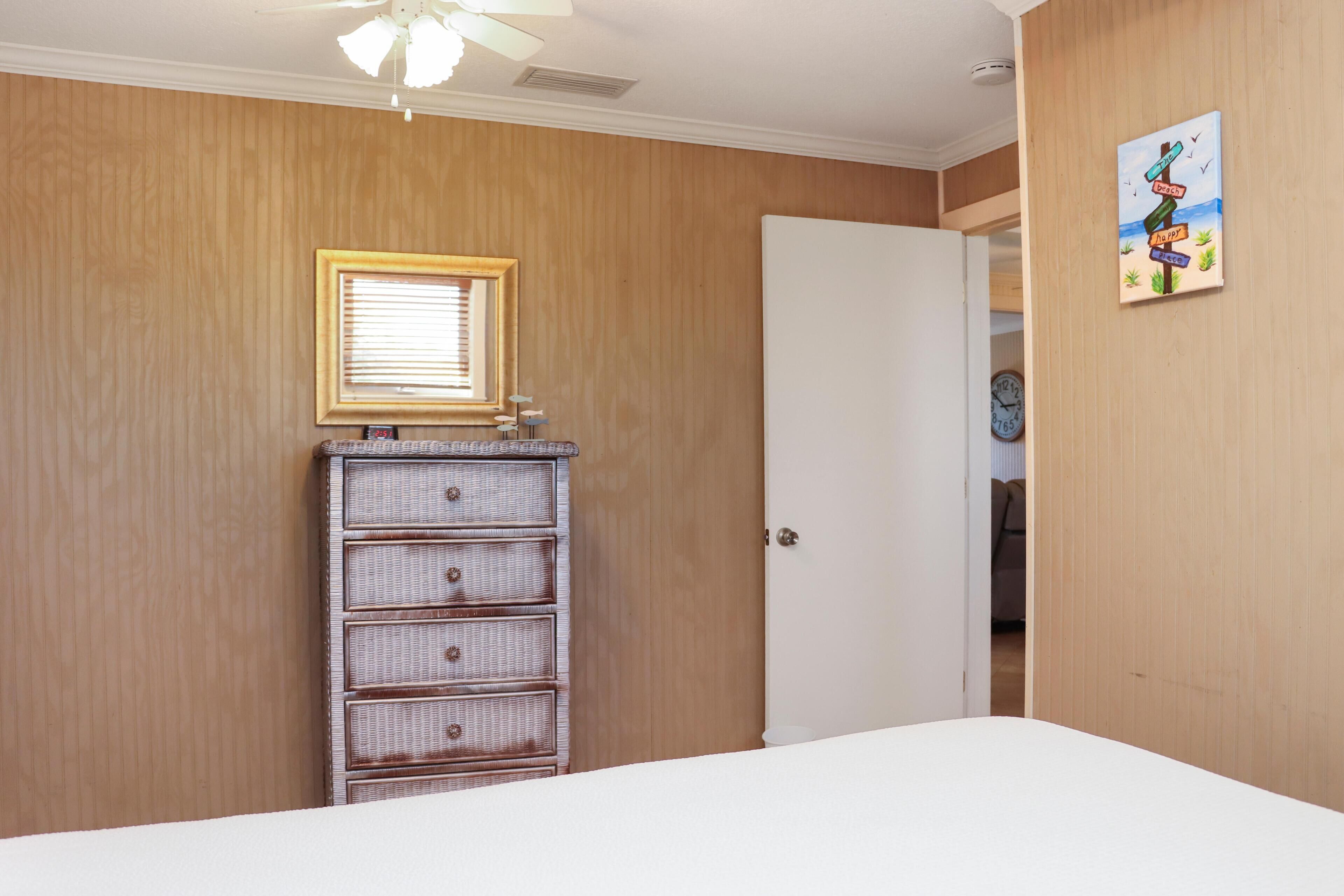 A bedroom with a wooden wall, a dresser, a bed, a window with blinds, and a door.
