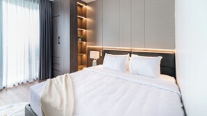 A modern hotel room with a large bed, built-in shelving, a bedside table with a lamp, and a view of the outdoors through sheer curtains. - Luxe Paradise Suites To Ngoc Van (Hanoi)
