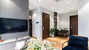 A modern living room with a flat-screen TV, wooden panel wall, and a dining area with a table and chairs. - Luxe Paradise Suites To Ngoc Van (Hanoi)
