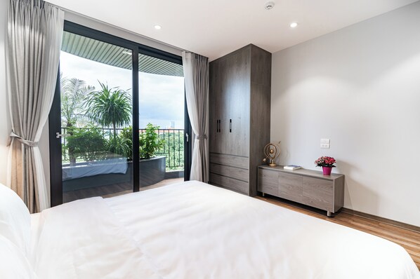 A bedroom with a large bed, a sliding glass door leading to a balcony, a wardrobe, and a bedside table with a lamp. - Luxe Paradise Suites To Ngoc Van (Hanoi)