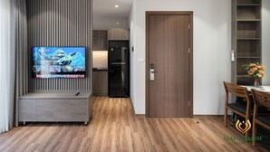 A modern living room with a flat-screen TV, wooden flooring, a built-in bench, a dining area with wooden chairs, and a kitchen in the background. - Luxe Paradise Suites To Ngoc Van (Hanoi)