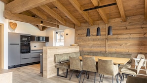 A modern kitchen with built-in appliances, a wooden accent wall, and a dining area with cushioned seating. - Superior Ferienhaus # 2B mit Sauna (Uttendorf)