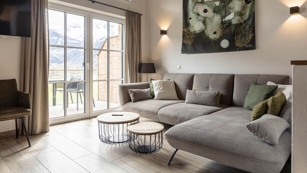 A modern living room with a grey sofa, two round coffee tables, a TV mounted on the wall, and a large window with curtains. - Superior Ferienhaus # 2B mit Sauna (Uttendorf)
