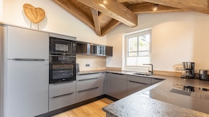 A modern kitchen with grey cabinets, a black countertop, and wooden ceiling beams. - Superior Ferienhaus # 2B mit Sauna (Uttendorf)