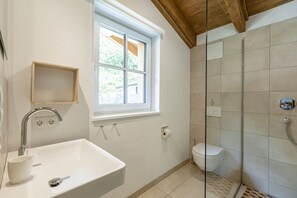 Une salle de bain avec un lavabo blanc, une fenêtre, une douche et des toilettes.