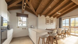 A modern kitchen with a large island, wooden ceiling beams, and a dining area with bar stools.