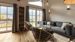 A spacious living room with a grey sofa, a wicker chair, and a glass cabinet.