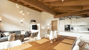 A modern living room with a wooden ceiling, a dining area with a wooden table, and a kitchen in the background.