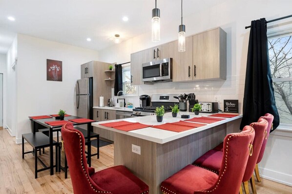 A modern kitchen with a central island, wooden cabinets, stainless steel appliances, and red upholstered chairs. - Modern Pilsen Apt 3 Bedrooms (Chicago)