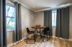 Relax in this serene space with a round table and two chairs, surrounded by natural light and a decorative wall piece.