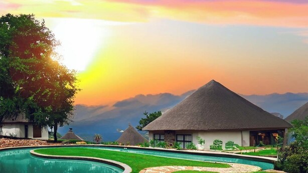 A resort with a swimming pool, thatched-roof huts, and a mountainous backdrop. - Indoni Eco Village  (Richmond)
