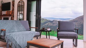 A modern living room with a sofa, armchair, and coffee table, a fireplace, and a large window with a mountain view. - Indoni Eco Village  (Richmond)