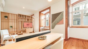 Een moderne hotelkamer met een houten eettafel, een televisiescherm, een houten roomdivider met planken en een groot raam met uitzicht.